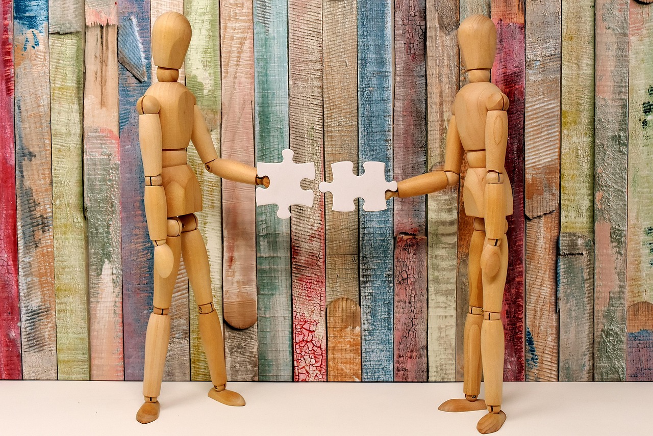 Deux personnages en bois assemblant des pièces de puzzle